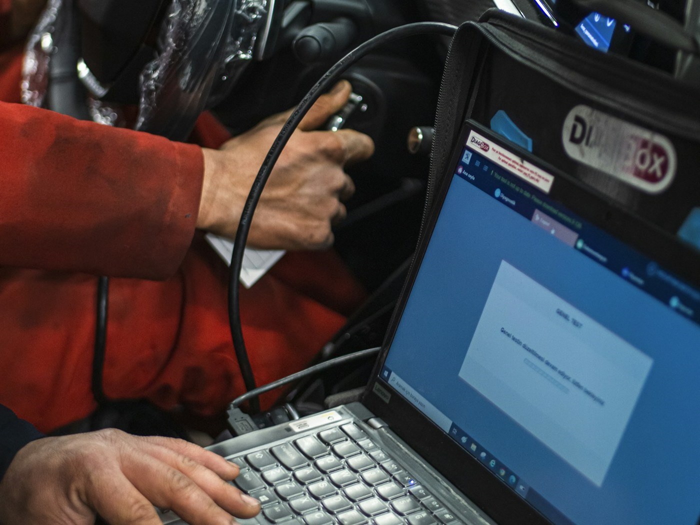 A technician running diagnostics on a laptop connected to a car