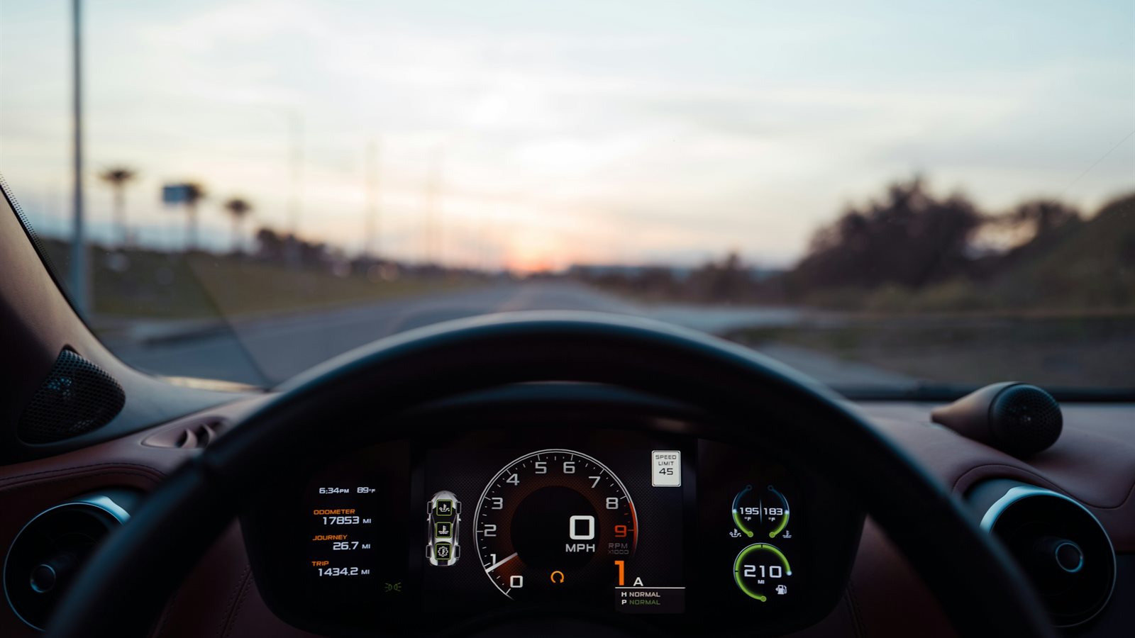 The view from the driver&rsquo;s seat of a car heading down a road at sunset