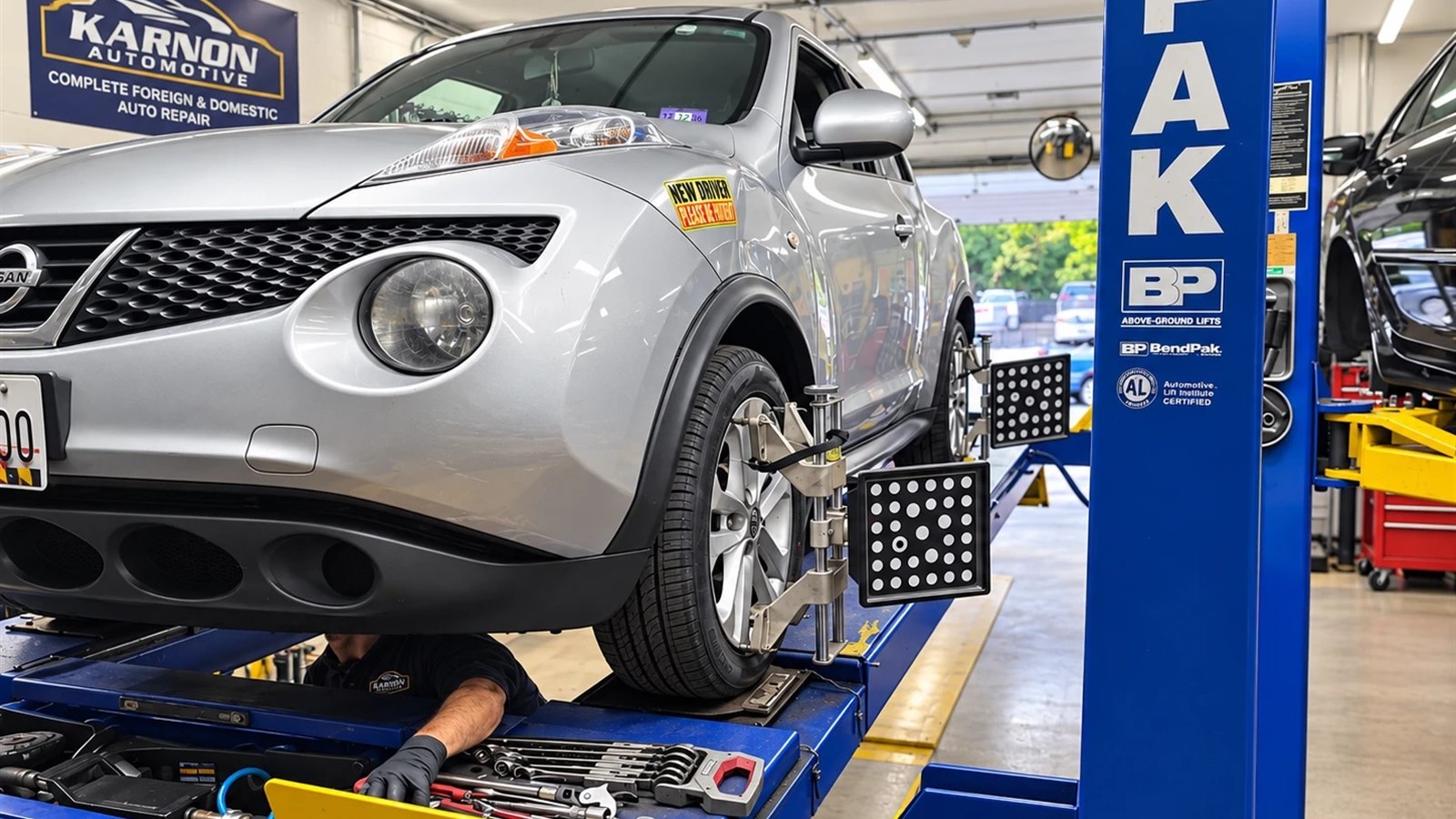 A Nissan up on the alignment lift with a technician working underneath it