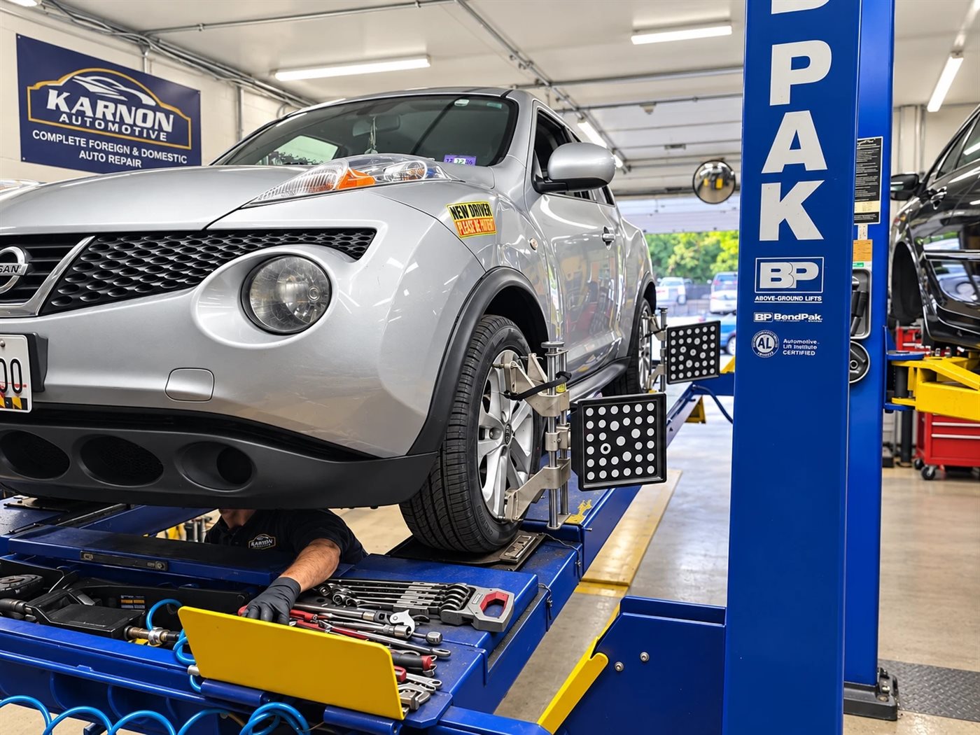 A Nissan up on the alignment lift with a technician working underneath it